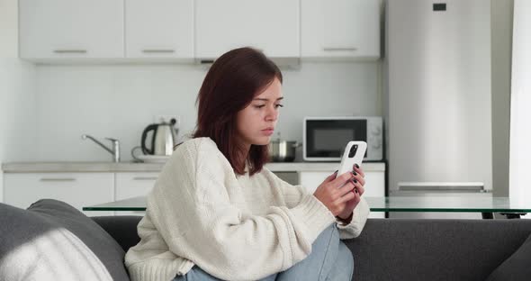 Portrait of an Upset Beautiful Young Caucasian Woman Using Smartphone at Home