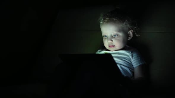 Little girl watching cartoons on a tablet in the dark