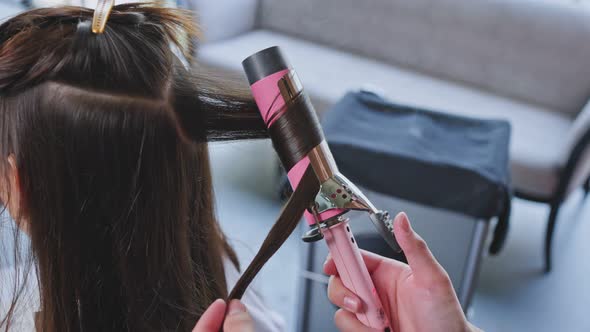 Close up of Expert man stylist's hand use curling iron make curly to young girl's in beauty salon.