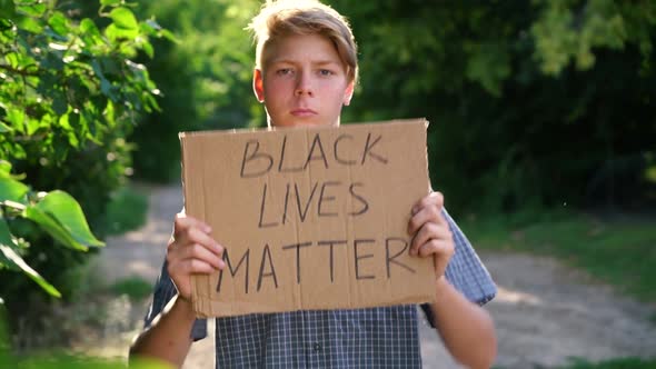 a Young Caucasian Teenager in a Blue Shirt Holds a Cardboard Box with Handwritten Text BLACK LIVES