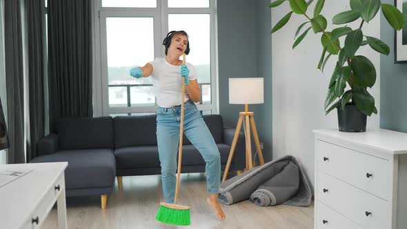 Woman in Headphones Cleans the House and Have Fun Singing with a Broom Like a Star at a Concert