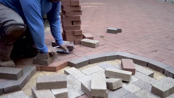 Brick paving expert fits brick paver into place and measures it and marks it for cutting while weari