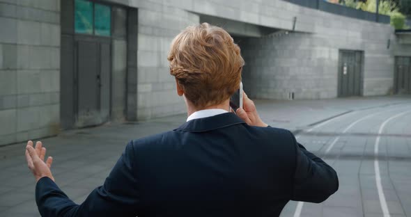 Rear View of Confident Young Businessman in Formal Suit Talking Phone While Walking at Downtown in