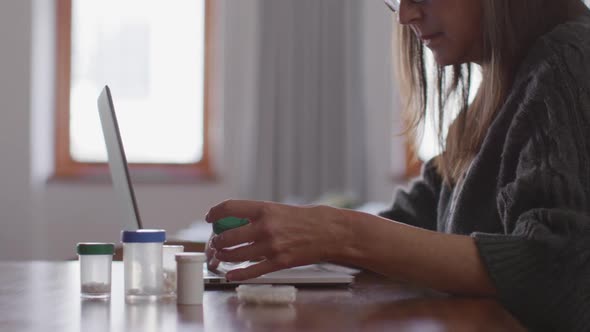 Woman holding medication container and using laptop at home