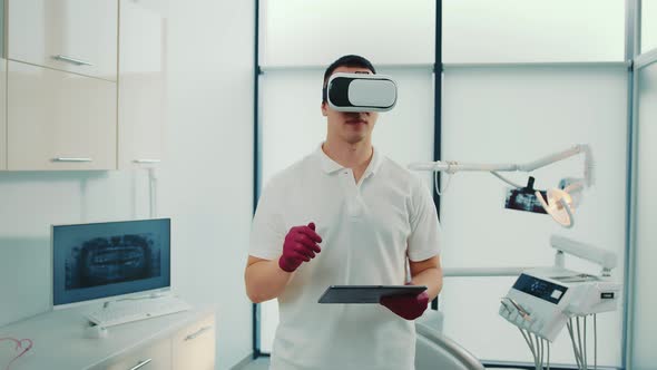 Front View of Young Dentist Holding Touchscreen Using Virtual Reality Glasses