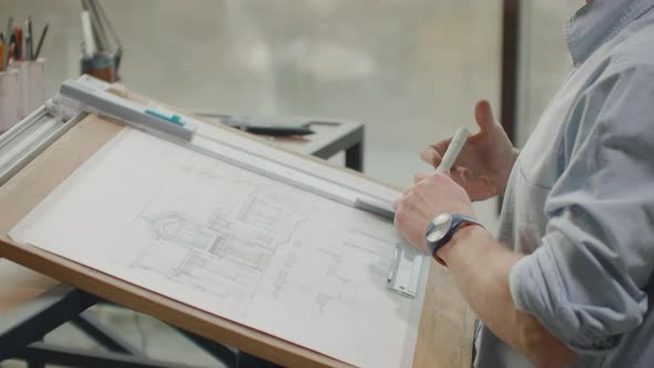 A Male Architect Sitting at a Table Draws a Plan of the Building and is Engaged in Design