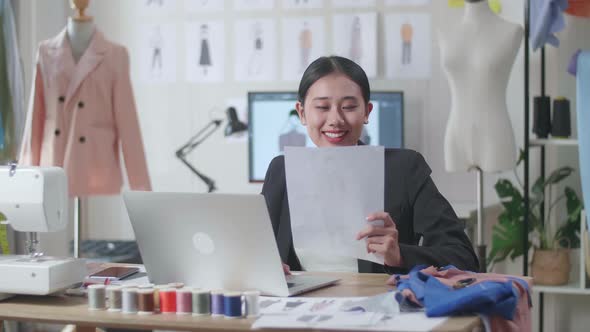 Smiling Female Designer In Business Suit Looking At The Paper In Hand And Comparing It To Laptop