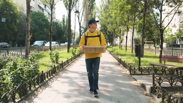 Courier of Food Delivery Service Holding Boxes of Pizza and Walking Down the Street