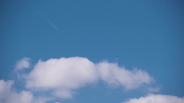 Distant Passenger Jet Plane Flying on High Altitude on Blue Sky with White Clouds Leaving Smoke