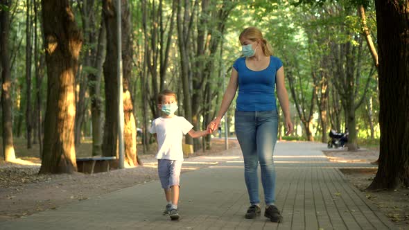 Mother and Son in Medical Masks Walk in the Park