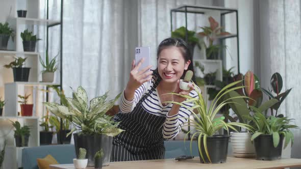 Smiling Asian Woman Holding Cactus Plant And Taking Photo By Smartphone At Home