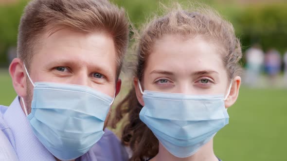 Bokeh Close Up Shot of Young Couple Wearing Safety Mask Looking at Camera Outdoors