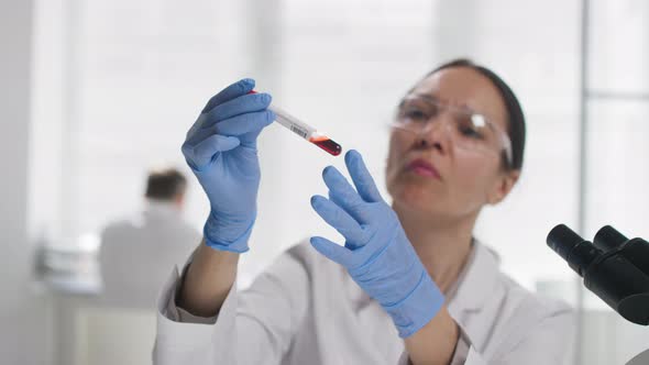 Female Scientist Looking at Test Tube with Blood Sample