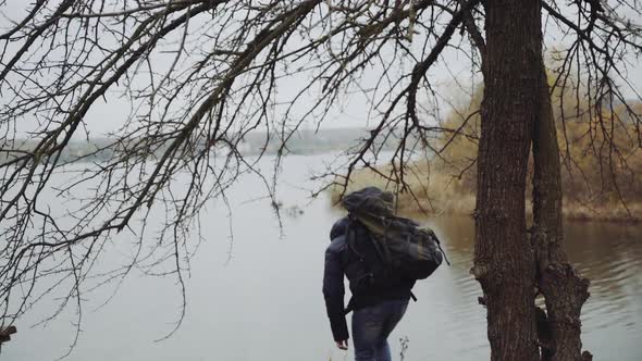 Tourist man enjoy nature. Traveler with backpack relaxing near river in forest