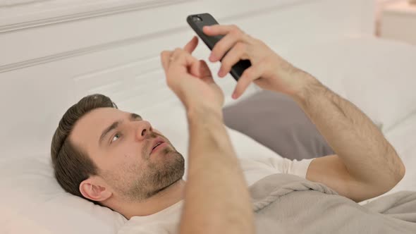 Smartphone Use By Young Man Laying in Bed