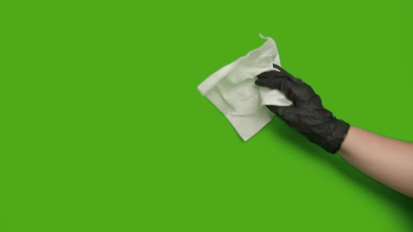 Female hand in a black rubber glove wipes with a paper napkin, green screen, chroma key