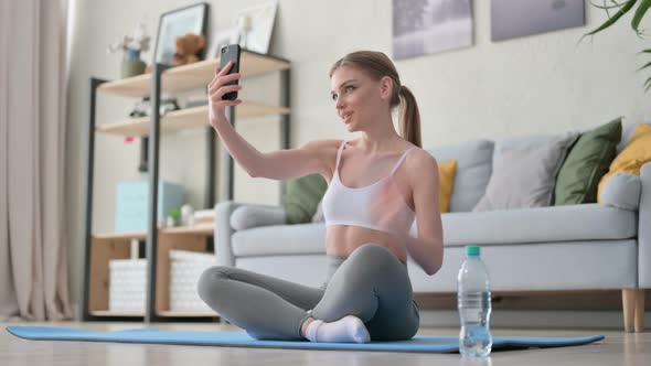 Young Woman Talking on Video Call on Smartphone While Sitting on Yoga Mat