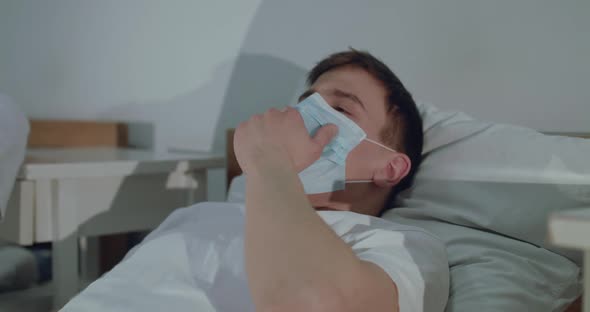 The Sick Young Man Coughing Through Mask on Hospital Bed