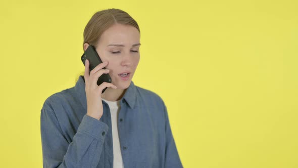 Young Woman Talking Angry on Phone on Yellow Background