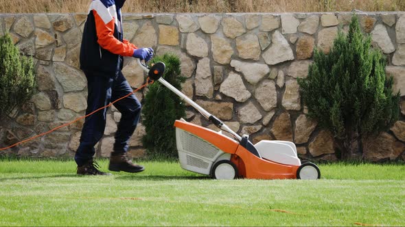 Lawn mower on green grass. A worker is cutting grass with an electric lawn mower