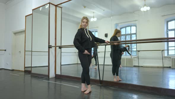 Concentrated Young Woman Rehearsing Dance Standing at Barre in Studio with People Reflecting in