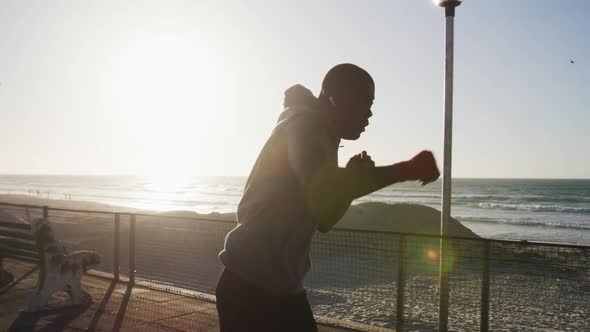 Focused african american man boxing and running, exercising outdoors by the sea