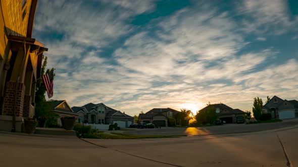 Sunset cloudscape over a suburban neighborhood with a US flag posted on one house - static time laps