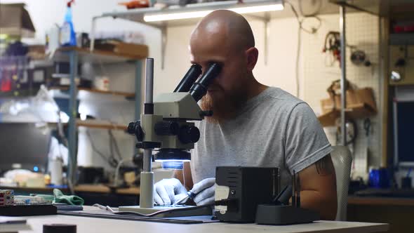 Technician Is Soldering Microchip Looking Through Microscope in Service Center