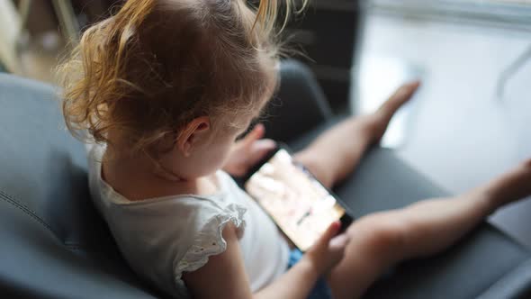 Smiling Little Girl is Sitting on Armchair and Using Smart Phone