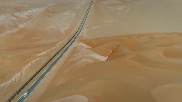 Aerial view of white car driving downhill in road in the desert, Abu Dhabi.