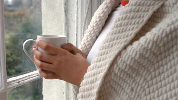 Woman with cup of coffee standing near window