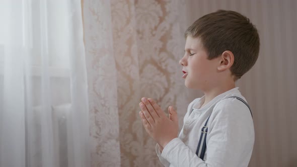 Male Christian Kid with Strong Faith in a Heart with Eyes Closed Holds His Hands Together and Prayed