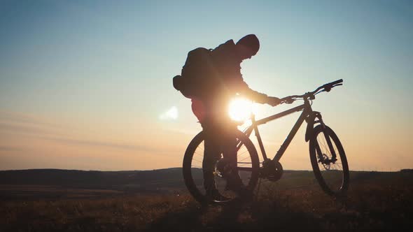 The Silhouette of the Mountain Bicycle Rider on the Hill with Bike at Sunset. Sport, Travel