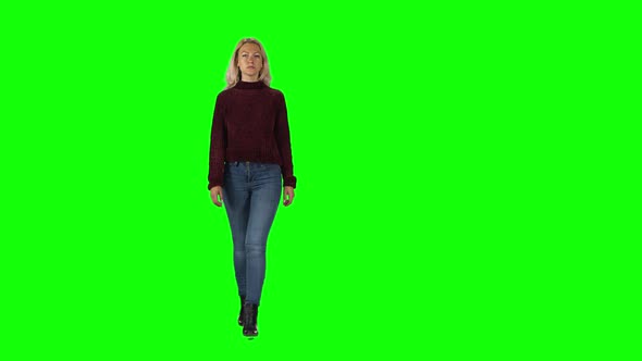 Blonde Girl in Pomegranate Sweater, Jeans and Boots Going Against a Green Screen.