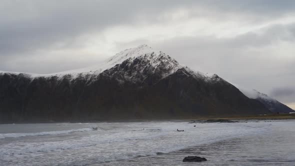 Surfers In Cold Sea Under Snow Capped Mountain