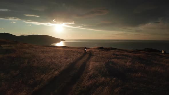 Biker Rides Enduro Motorcycle on Dirt Road Against of Sunrise Sea and Rocks