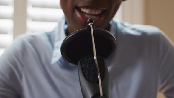 African american woman wearing headphones singing in microphone at home