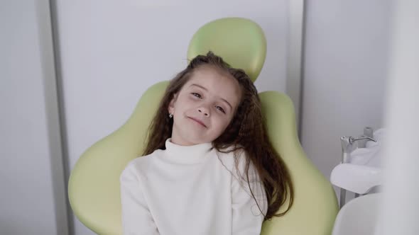 Happy Little Girl Smiling at Camera in Dental Chair of Pediatric Clinic