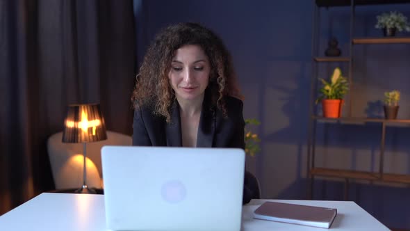 Female Manager in Black Business Suit Uses Laptop While Sitting at Table in Cozy Office
