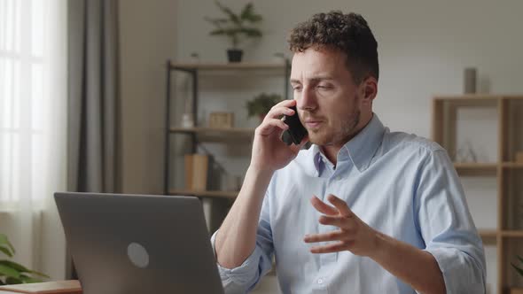 Attractive Young Businessman Sit at Desk Use Laptop Discuss Project Details with Colleague By Phone