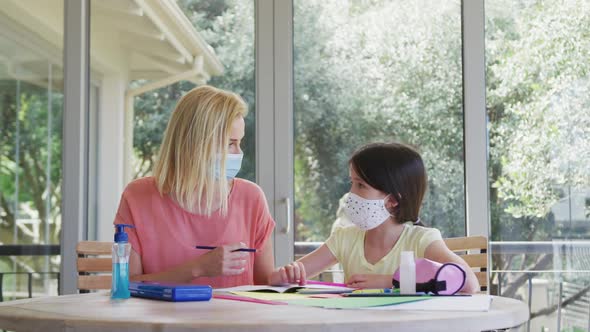 Mother wearing face mask helping daughter with homework at home