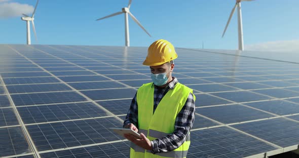 Worker man with digital tablet  wearing safety mask inside solar panels farm