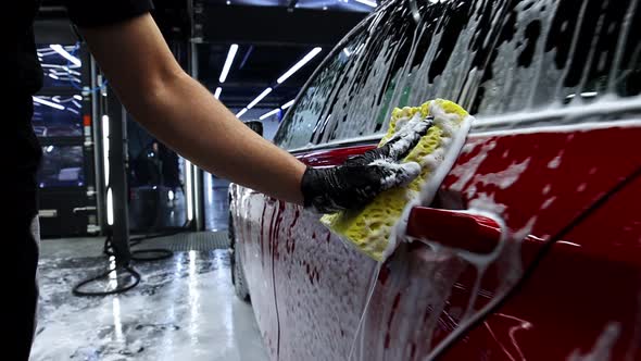 A Man Holds a Sponge Along the Car Covered with Foam