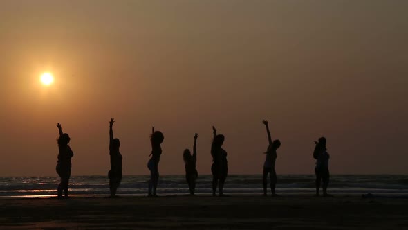 People stretching at a sandy beach in Goa at sunset.