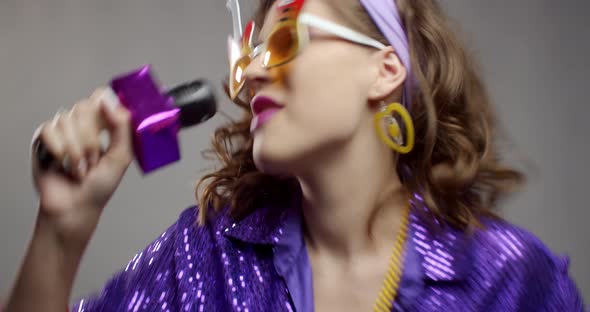 Close up of a young woman in silly glasses singing at the retro party, 4k