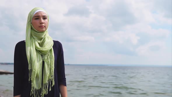 A Young Muslim Woman in a Veil Comes with a Pensive Look Along the Sea