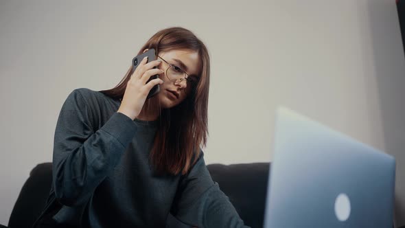 The Young Redhead Freelancer Writes on Her Laptop What is Dictated to Her By Phone