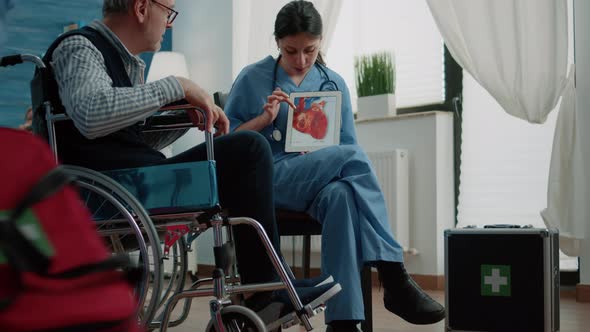 Old Patient with Handicap Looking at Heart Figure on Tablet