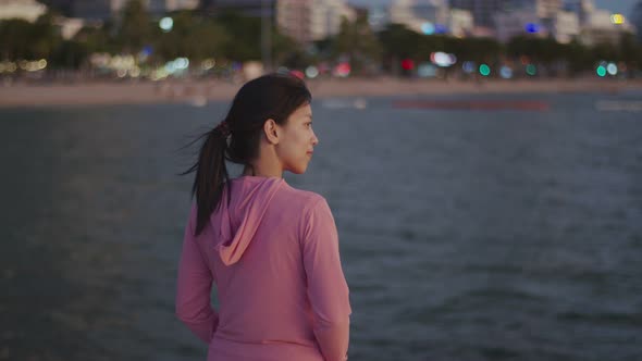 A beautiful Asian female runner looks at the sea view while standing on the beach.