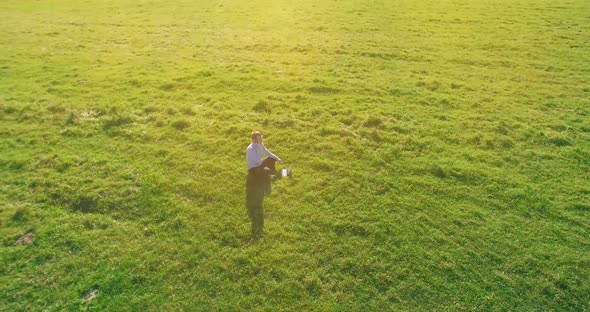 Low Orbital Flight Around Man on Green Grass with Notebook Pad at Yellow Rural Field